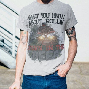 May include: A gray t-shirt with a graphic print of a person riding a motorcycle. The text on the shirt reads "What you know about rollin' down in the deep".