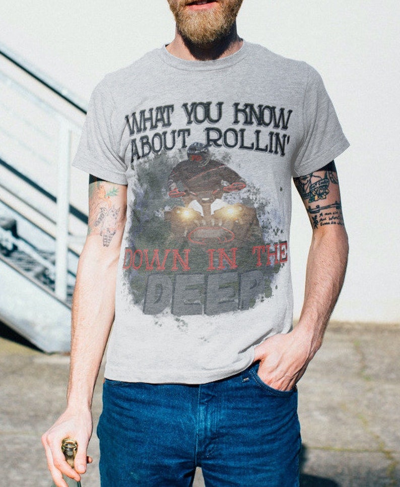 May include: A gray t-shirt with a graphic print of a person riding a motorcycle. The text on the shirt reads "What you know about rollin' down in the deep".