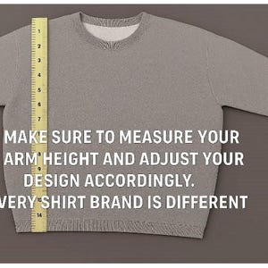 May include: A light gray crewneck sweatshirt featuring a yellow measuring tape placed vertically along the left side, showing a length of 14 inches. The text reads: MAKE SURE TO MEASURE YOUR ARM HEIGHT AND ADJUST YOUR DESIGN ACCORDINGLY. EVERY SHIRT BRAND IS DIFFERENT.