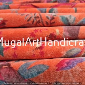 May include: A stack of orange fabric with a floral pattern. The fabric has a soft, velvety texture. The text "MugalArtHandicraft" is printed on the fabric.