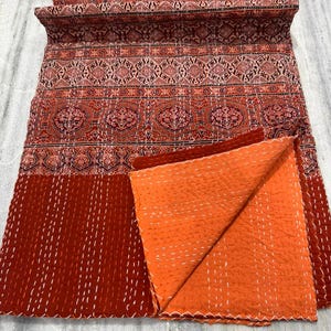 May include: A red and orange kantha quilt with a floral pattern. The quilt is made of cotton and is hand-stitched. It is a traditional Indian textile.