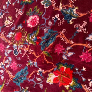 May include: A close-up of a burgundy velvet fabric with a floral pattern. The flowers are in shades of red, pink, blue, and green.