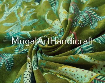 May include: Green velvet fabric with a printed design of leaves and animal silhouettes. The fabric has a soft, plush texture.