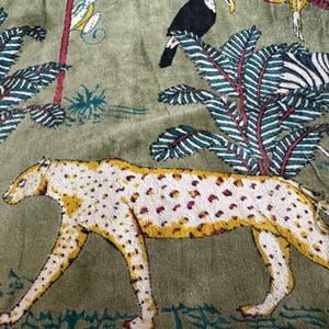May include: A green fabric with a white and yellow cheetah print. The cheetah is walking to the right. The background is a green fabric with a white and green floral pattern.
