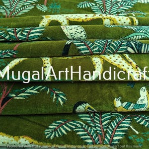 May include: Green fabric with a repeating pattern of leopards, birds, and leafy branches. The fabric has a velvet texture and is folded in layers. The text "Mugal Art Handicraft" is visible in the center of the image.