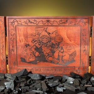 May include: A wooden three-panel folding dice tray with a goblin illustration and the text "Dice Goblin 8.58". The tray has a brown wood finish and features a goblin sitting on top of dice. The goblin is holding a hammer and has a mischievous expression. The tray is surrounded by black charcoal.