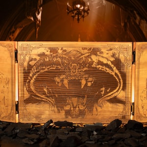 Könnte beinhalten: Ein dreiteiliger Holzschirm mit aufwendigen Laserschnitt-Designs. Das Mittelteil zeigt eine Kreatur mit scharfen Zähnen, während die Seitenteile Figuren zeigen. Der Schirm ist aus hellem Holz gefertigt und hat Metallringgriffe.