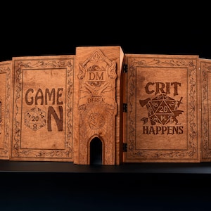May include: A wooden tabletop gaming screen with engraved designs and text. The screen features phrases like "GAME ON," "CRIT HAPPENS," and "HOW I ROLL." The central panel is engraved with "DM" and the name "DEREK."