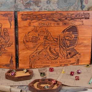 May include: A brown wooden Dungeon Master screen with engraved artwork and the text "Beware the Smiling Dungeon Master." The screen has a hinged design. Dice trays and dice are visible in the foreground, along with a map and small glass bottles.