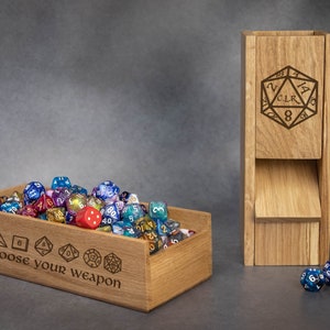 Puede incluir: Caja de madera llena de dados de colores, con el texto "choose your weapon" grabado en la parte delantera. Una caja de madera separada con un solo dado grabado en la parte delantera.