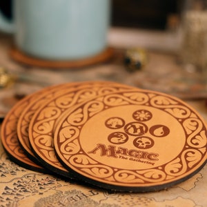 May include: Four brown leather coasters with a decorative border and the Magic: The Gathering logo in the center. The logo features the five mana symbols and the words "Magic: The Gathering".