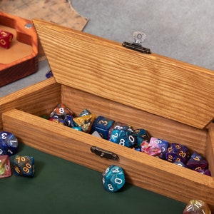 May include: A wooden box with a hinged lid, filled with colorful dice. The box has a lock and key. The dice are scattered on a green felt surface.