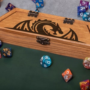 May include: A wooden box with a green felt interior and a dragon design on the lid. The box is filled with colorful dice, including a blue d20, a red d6, and a green d12.
