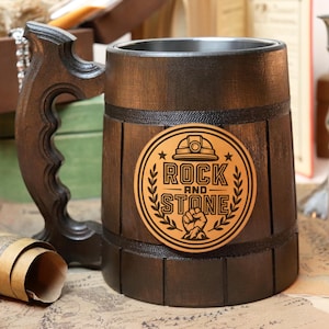 May include: A dark brown wooden beer stein with a decorative handle. The stein features a circular emblem with the words "ROCK AND STONE" and a miner's helmet and fist. The stein is surrounded by other vintage items.