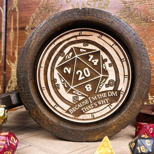 May include: Dark brown wooden mug with a laser-etched D20 die design and the text "BECAUSE I'M THE DM THAT'S WHY". The mug has a light wood interior. Dice of various colours are scattered around the mug.
