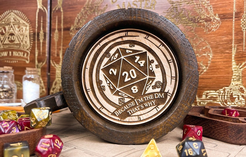 May include: Dark brown wooden mug with a laser-etched D20 die design and the text "BECAUSE I'M THE DM THAT'S WHY". The mug has a light wood interior. Dice of various colours are scattered around the mug.