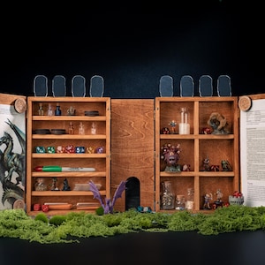 May include: A wooden tabletop gaming organizer with multiple shelves and compartments. It features dice, miniature figurines, and potion bottles. The organizer is open, revealing printed pages and a dragon sculpture, set against a black background.
