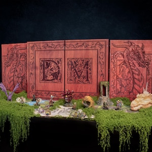 Puede incluir: Una pantalla de DM de madera marrón rojizo con ilustraciones de dragones y las letras "DM". Figuras en miniatura y una calavera de dragón están dispuestas sobre una superficie cubierta de musgo, creando una escena de juego de fantasía.
