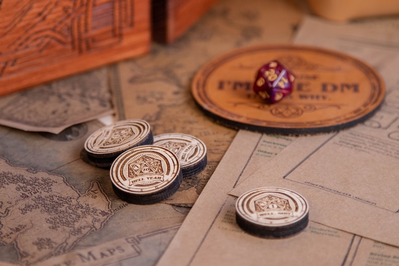 May include: A collection of tabletop gaming accessories, including wooden tokens, a leather coaster with text, and a multi-sided die. The tokens have a laser-etched design with the words "HELL YEAR". The coaster reads "I'M THE DM, WHY?"