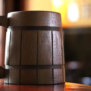 May include: A dark brown wooden beer stein with a handle. The stein has a barrel-like design with horizontal grooves.