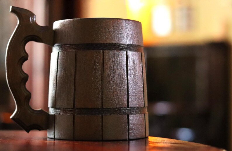 May include: A dark brown wooden beer stein with a handle. The stein has a barrel-like design with horizontal grooves.