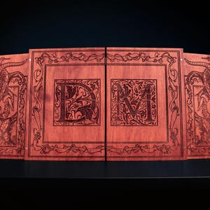 May include: A wooden game board with a reddish-brown finish. The board is divided into four panels, with dragon illustrations on the outer panels and the letters "DM" in the center. Intricate floral designs and borders frame the artwork.