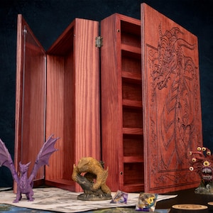 May include: A wooden tabletop game organizer with a hinged design. The organizer is made of reddish-brown wood and features a carved dragon design on the front. Miniature figurines and dice are displayed on a game mat.