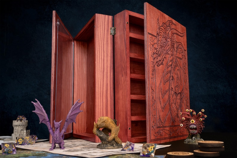 May include: A wooden tabletop game organizer with a hinged design. The organizer is made of reddish-brown wood and features a carved dragon design on the front. Miniature figurines and dice are displayed on a game mat.
