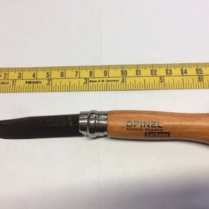 May include: A brown wooden handled pocket knife with a black blade and a silver metal bolster. The knife is labeled "OPINEL, SAVOIE FRANCE, Carbone".