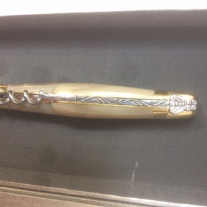 May include: A gold and ivory pocket knife with a corkscrew and a decorative design on the handle.