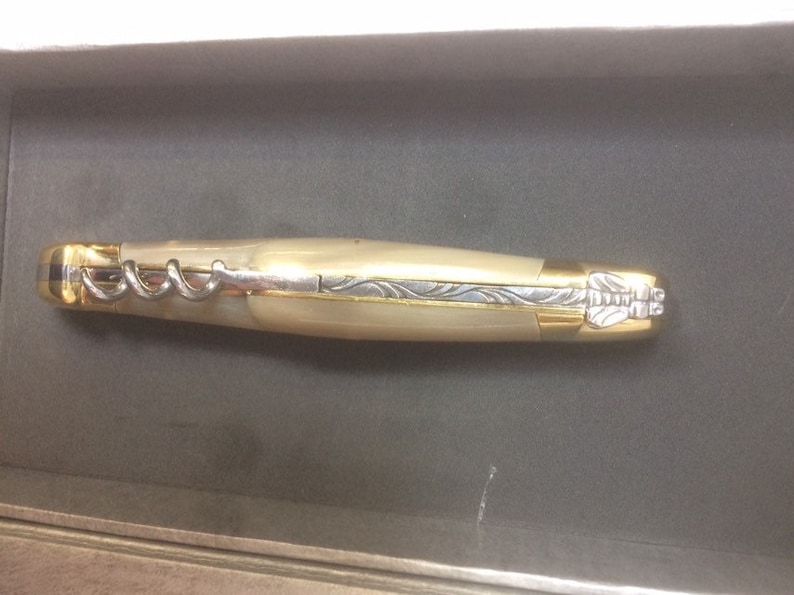 May include: A gold and ivory pocket knife with a corkscrew and a decorative design on the handle.