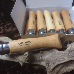以下が含まれることがあります： 木製のハンドルが付いた Opinel 折りたたみナイフ 8 本入りボックス。ナイフは、Opinel ロゴと「Savoie, France」の文字が書かれた白い箱に入っています。