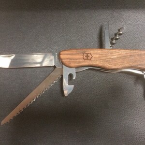 Peut inclure: Un couteau suisse multifonction avec un manche en bois. Le couteau comprend une lame, une scie, un ouvre-bouteille, un tire-bouchon et un crochet.