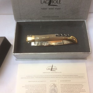 May include: A Laguiole pocket knife with a bone handle and gold accents, in a gray box with a certificate of authenticity. The certificate states that the knife was handcrafted in the village of Laguiole, France.