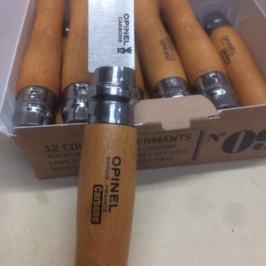May include: A box of 12 Opinel No. 08 folding knives with carbon steel blades and wooden handles. The box is labeled "Opinel No. 08, 12 Col, Acier Haute Lame 9 cm, Manche Bois Teinte"