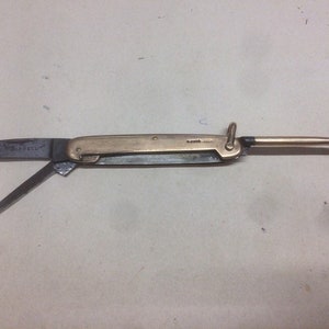 May include: A vintage pocket knife with a brass handle and a blade that folds out. The knife has a small hook on the end of the handle.