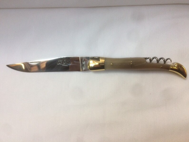 May include: A silver pocket knife with a brown handle and a corkscrew. The knife has a gold-colored metal accent on the handle.