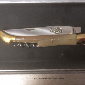 May include: A gold and ivory pocket knife with a corkscrew and the words "Forge de Laguiole" engraved on the blade.