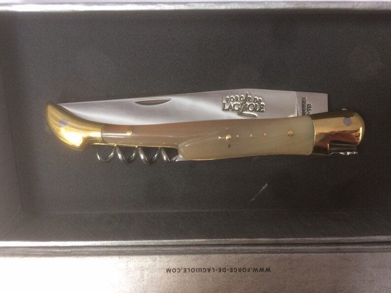May include: A gold and ivory pocket knife with a corkscrew and the words "Forge de Laguiole" engraved on the blade.
