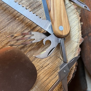 May include: A multi-tool with a wooden handle and various tools, including a saw, a fork, a bottle opener, a corkscrew, and a pair of scissors. The tools are made of metal and have a silver finish.