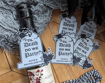 May include: Four black and white tombstone-shaped gift tags with the text "Til Death Do We Party!" and "Katie's Bachelorette" printed on them. The tags are tied with black and white twine to a small bottle of prosecco.