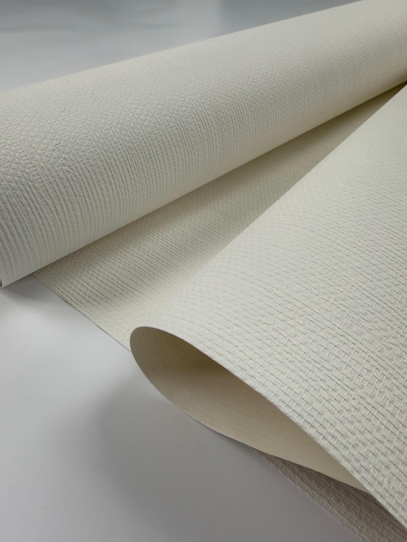 Puede incluir: Primer plano de un rollo de papel tapiz blanco texturizado. El papel tapiz tiene un patr&oacute;n tejido sutil.