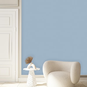 May include: A white armchair with a rounded back and a white side table with a decorative base. The chair and table are in front of a light blue wall.