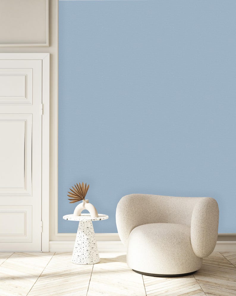 May include: A white armchair with a rounded back and a white side table with a decorative base. The chair and table are in front of a light blue wall.