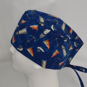 Può includere: Un cappello chirurgico blu con un tema nautico. Il cappello presenta un motivo di fari bianchi, bandiere arancioni e bianche e ancore su uno sfondo blu scuro. Il cappello ha lacci sul retro per la regolazione.