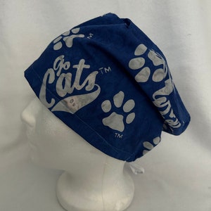 May include: A blue scrub cap with white paw prints and the words "Go Cats" printed on it. The cap is made of a soft fabric and has ties in the back for a secure fit. The cap is designed to be worn in a medical or veterinary setting.