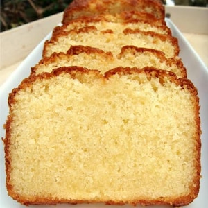 May include: A loaf of golden-yellow pound cake sliced into several thick, uniform pieces. The cake has a porous, moist crumb texture with a slightly darker, browned crust along the top edges, arranged neatly in a row on a white serving platter.