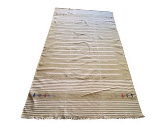 May include: A rectangular, beige and white striped rug with a fringed edge. The rug has horizontal stripes and small embroidered details in red, blue, and black. The rug is displayed on a white background.