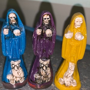 Peut inclure: Trois petites figurines en céramique de squelettes portant des robes. Les figurines sont peintes en bleu, violet et jaune. Chaque figurine tient une petite sphère dans ses mains.