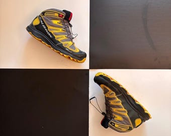 May include: A black, grey, and yellow hiking boot with the brand name "Salomon" visible. The boot has a high-top design with a lace-up closure and a textured sole. The boot is designed for outdoor activities.